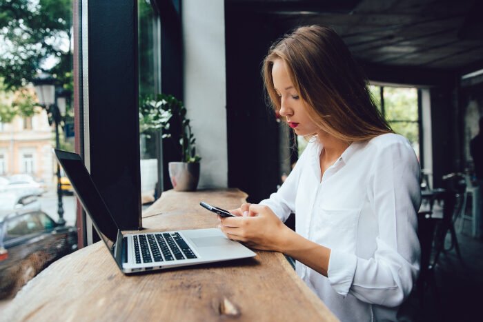 Beautiful woman using a smartphone, while sitting with laptop, at cafe